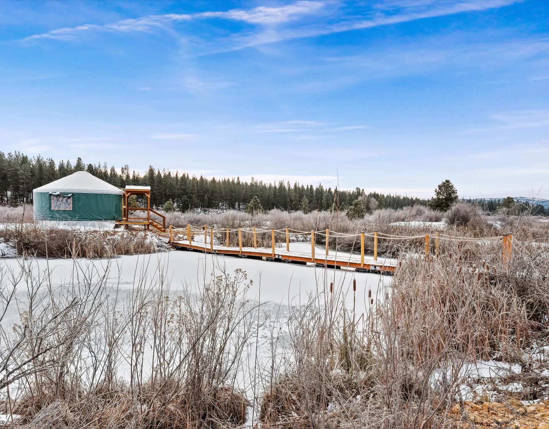 Image shows a wintertime view of bridge over beaver pond to yurt.